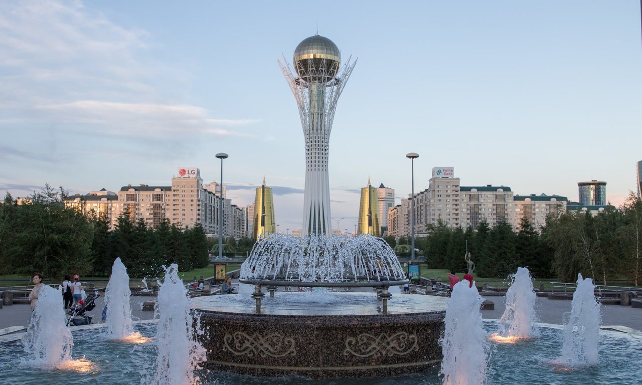 The Baiterek monument rising above lit fountains in Astana, Kazakhstan, at dusk