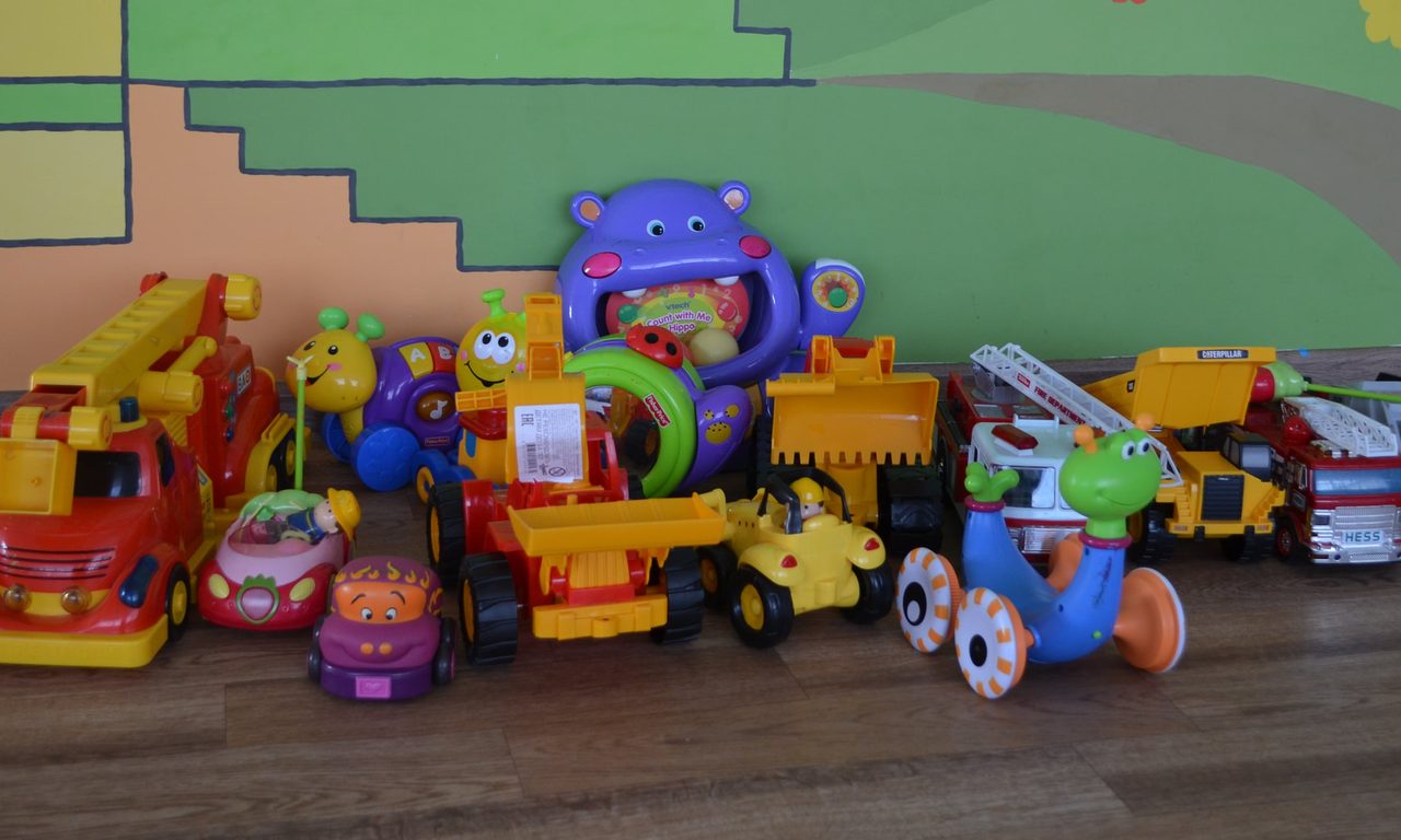 A row of donated ride-on toys, trucks and activity toys lined up against a painted mural wall at the babyhouse