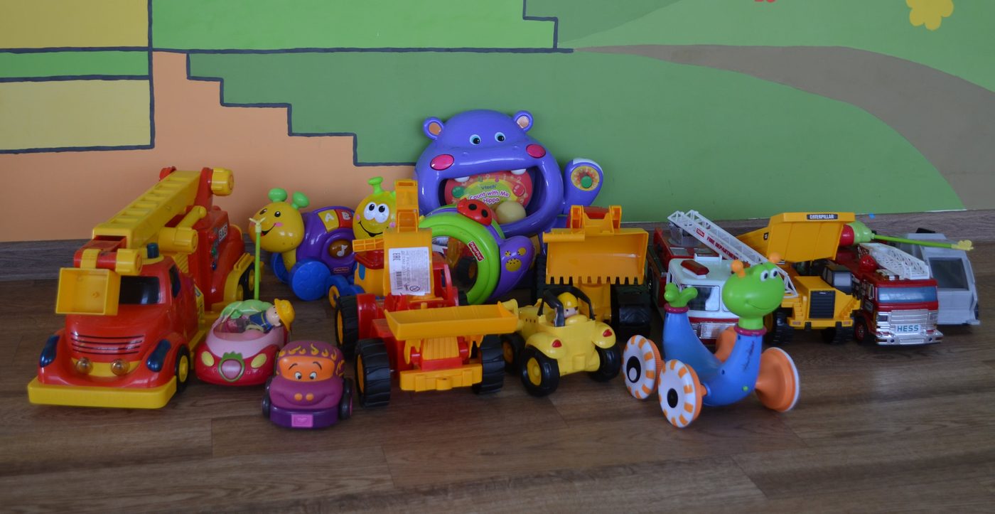 A row of donated ride-on toys, trucks and activity toys lined up against a painted mural wall at the babyhouse