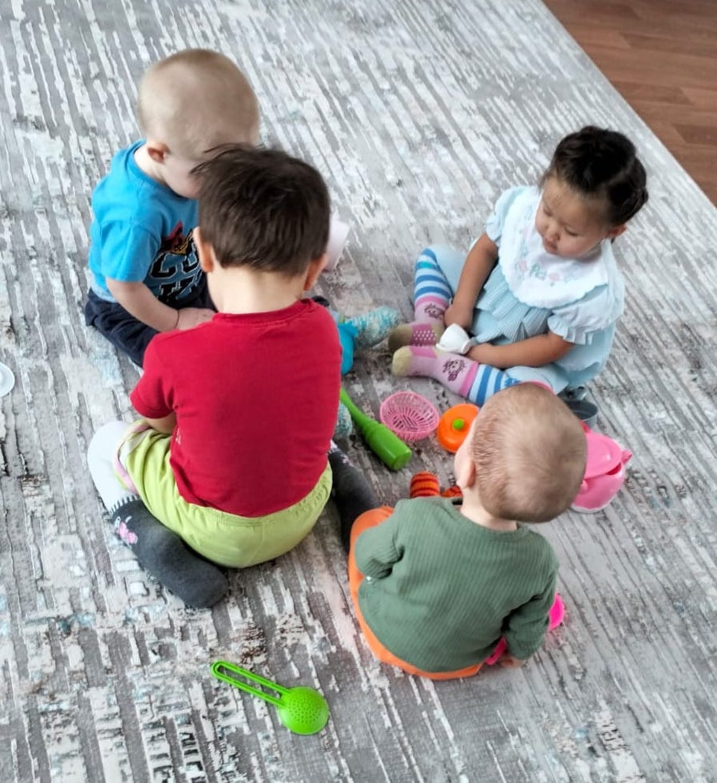 Four toddlers sitting and playing with toys on the new grey patterned carpet