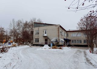 The two-storey pale brick Shchuchinsk Babyhouse building in winter, with a snow-covered yard and playground