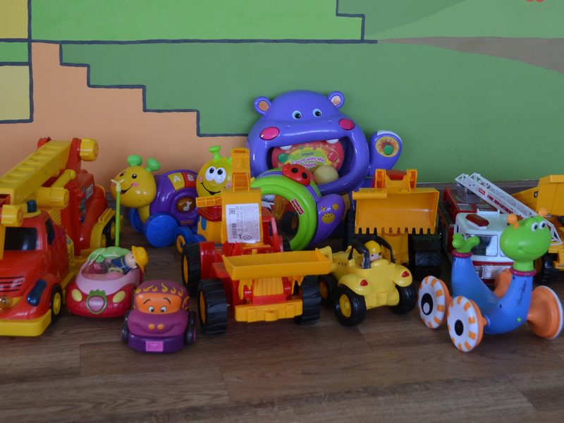 A row of donated ride-on toys, trucks and activity toys lined up against a painted mural wall at the babyhouse