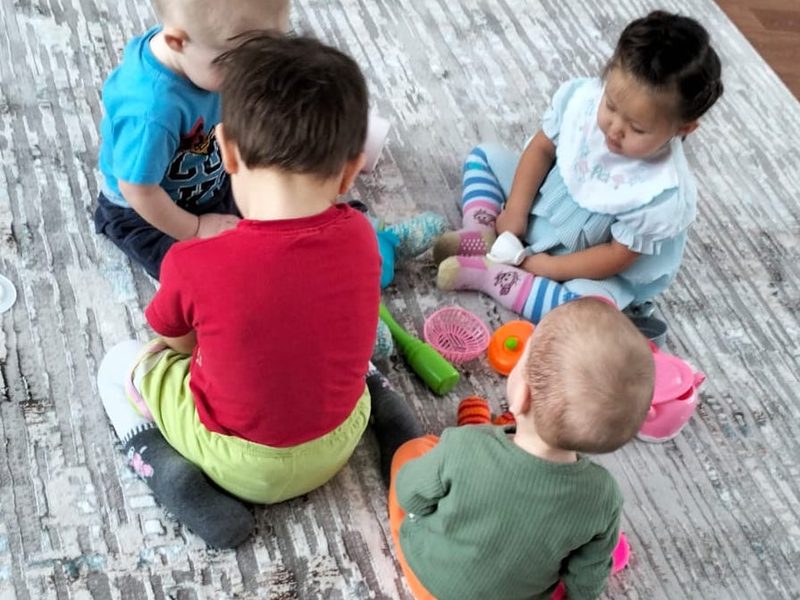 Four toddlers sitting and playing with toys on the new grey patterned carpet